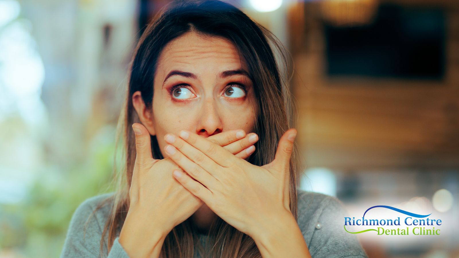 Woman covering mouth with hands, eyes wide with surprised expression.